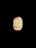 Top view of a cream and tan stone scarab showing incised wing cases and head details against a black background.