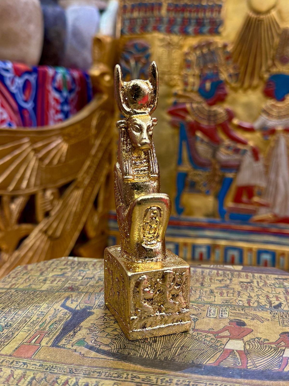 Front angled view of the gold finish Hathor kneeling statue with horns, sun-disc headdress and decorated square base.
