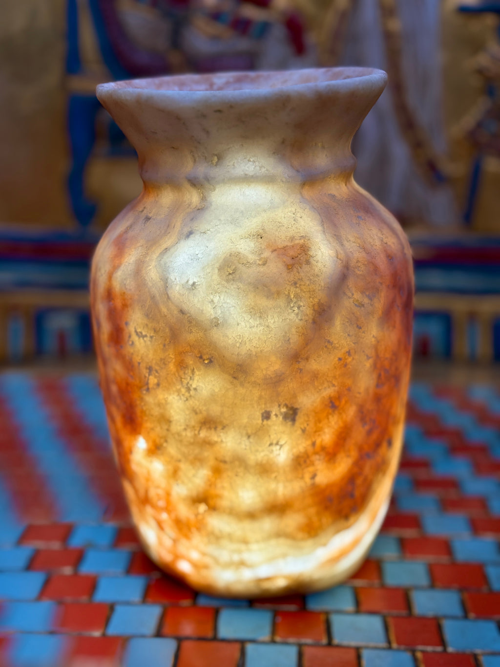 Small curved alabaster vase with cream and taupe markings and a softly flared cup-shaped rim — illuminated view.