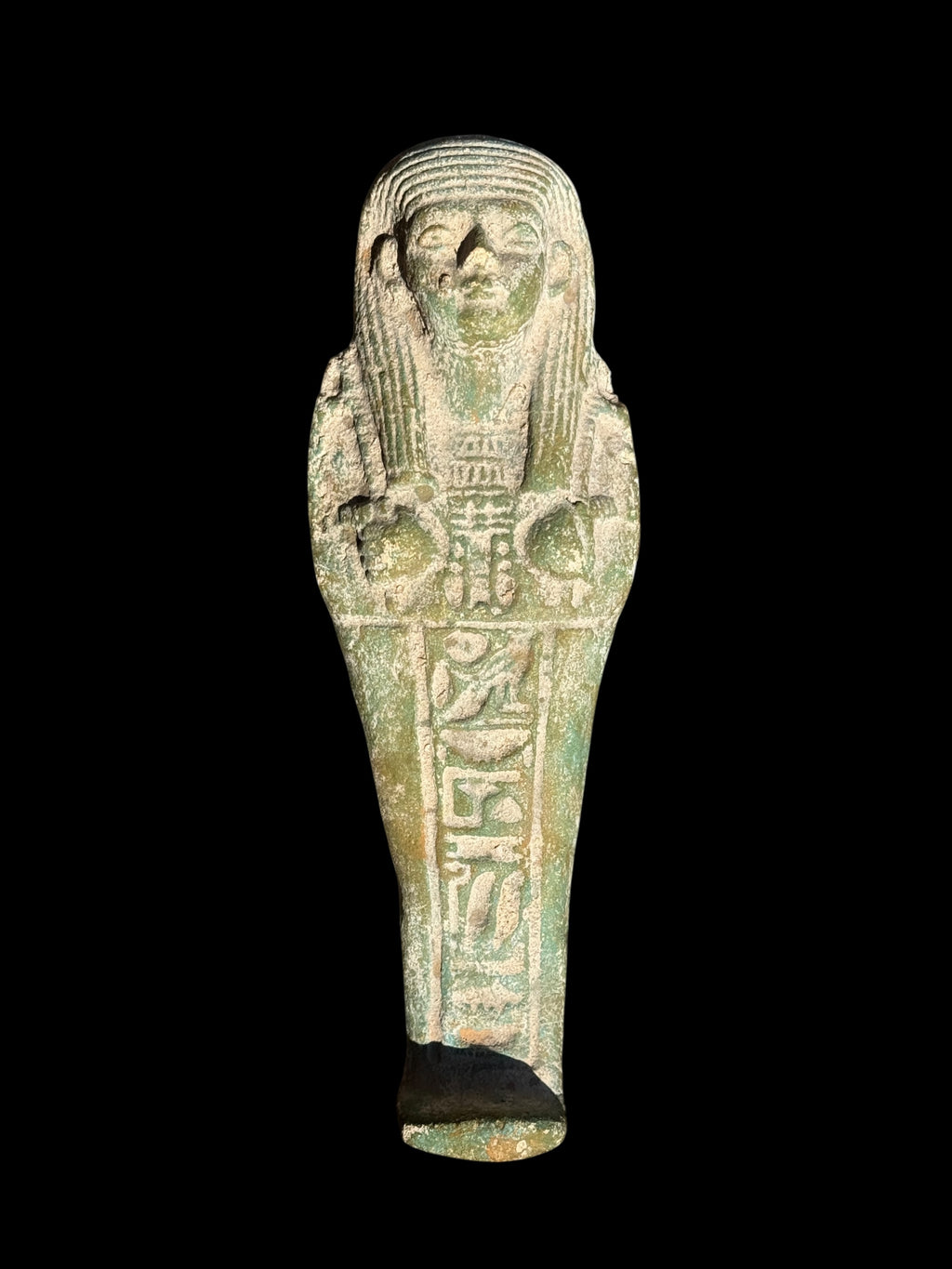 Front view of a green and pale mottled shabti figurine with a striped wig, crossed arms and a vertical panel of hieroglyphic details.