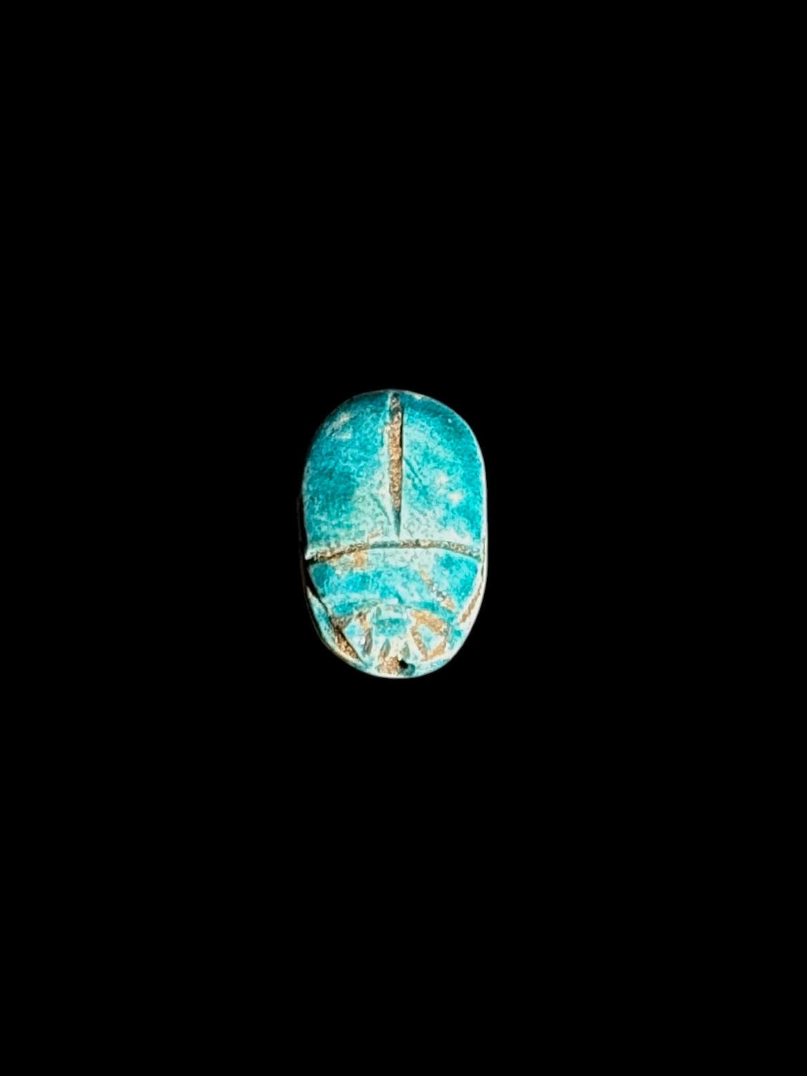 Top view of a turquoise-coloured stone scarab with incised beetle details, pale patches and tan accents against a black background.