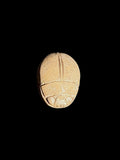 Rounded tan stone scarab back showing a central wing division and outlined head details against a black background.