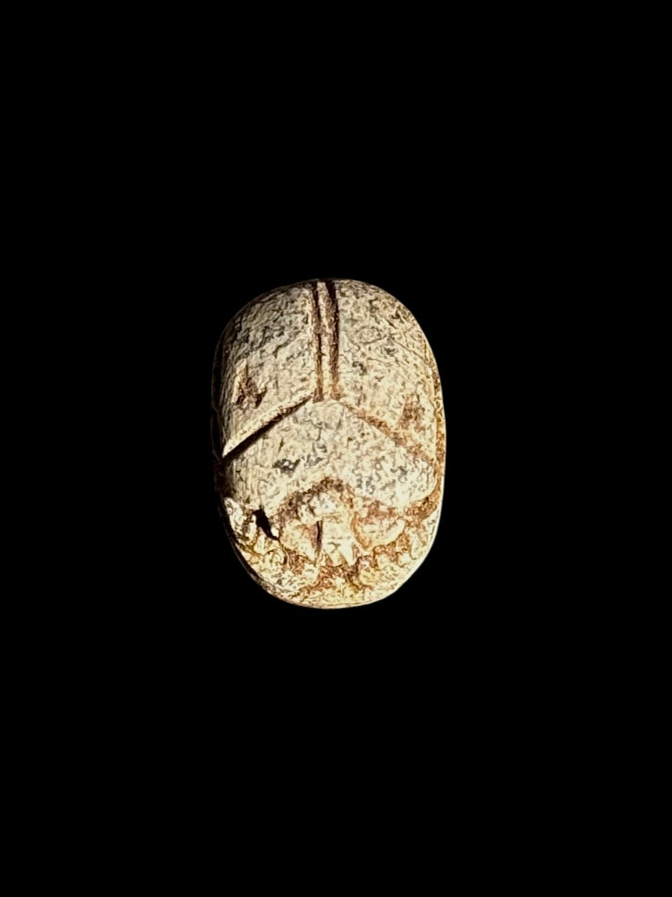 Top view of a cream and brown mottled stone scarab with incised beetle details against a black background.