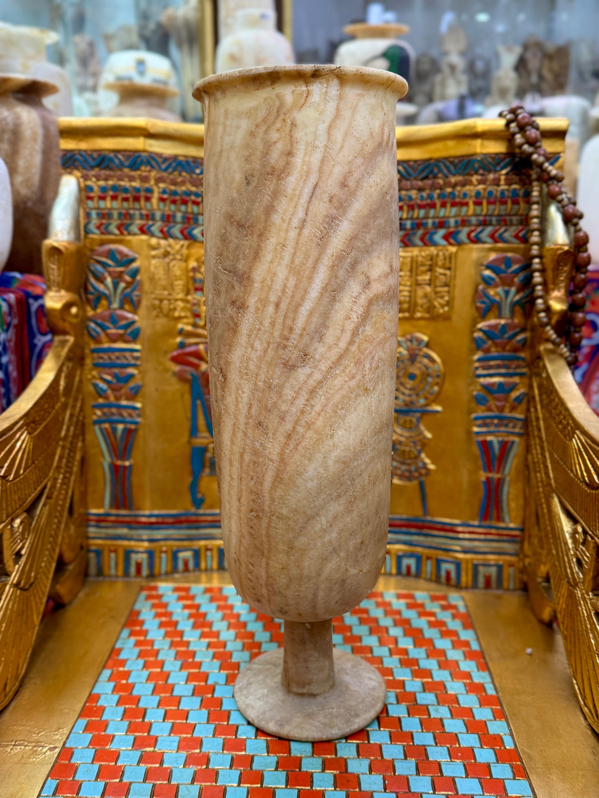 Tall cylindrical alabaster pedestal vase with flowing cream and honey-coloured ribbons, short stem and round foot — unlit full view.