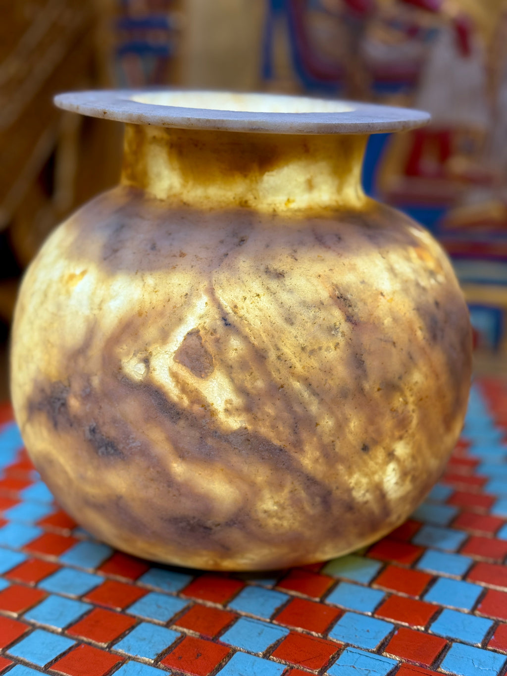Rounded taupe and cream alabaster vase with sweeping markings, a short neck and wide flat rim — illuminated view.