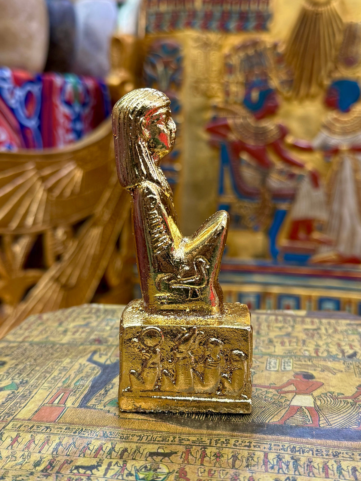 Side view of the gold finish Isis kneeling statue with sculpted headdress and decorated square base.