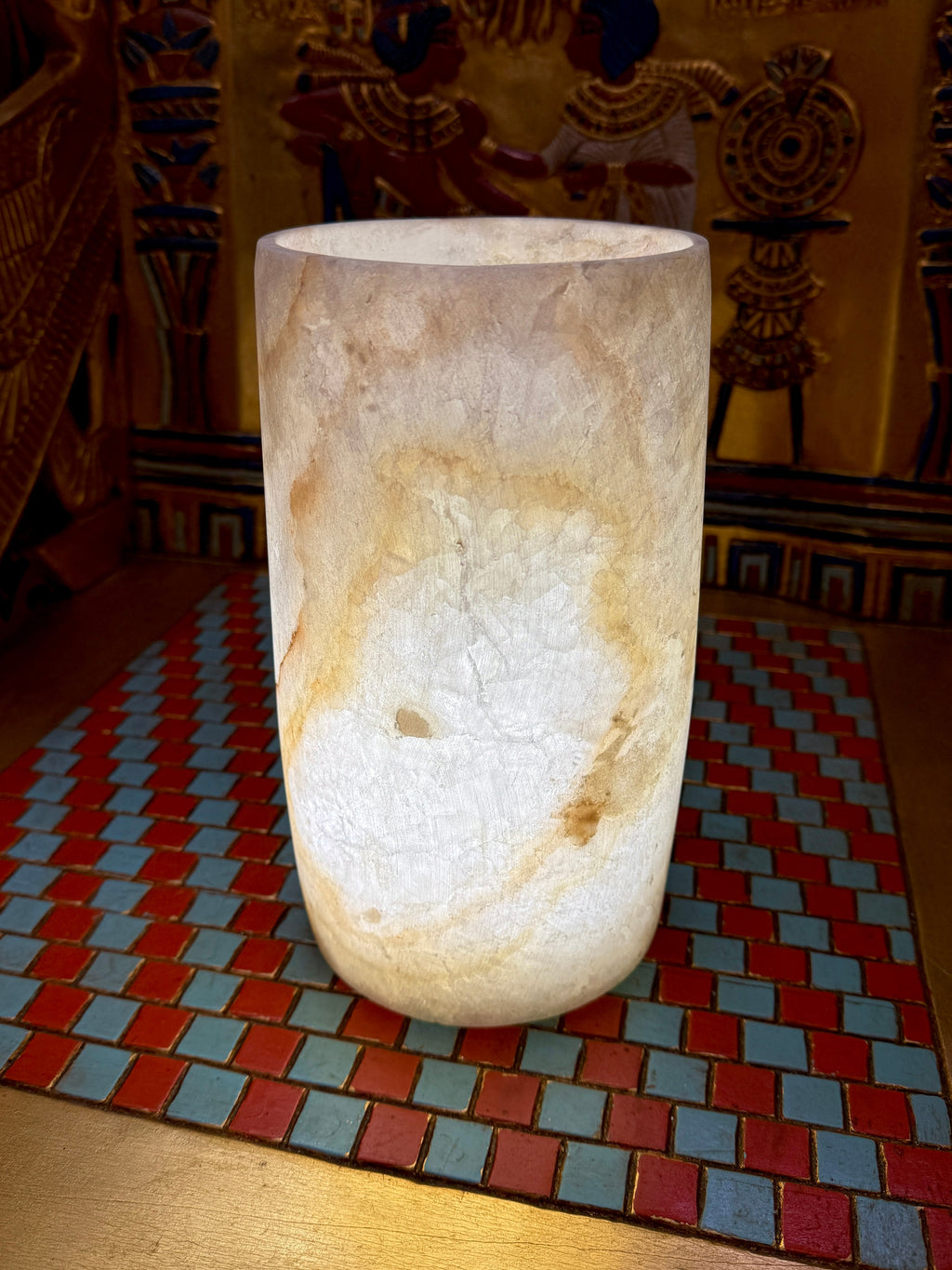 Slender cream alabaster cylinder vase with a rounded base and sweeping honey-coloured vein — full view.