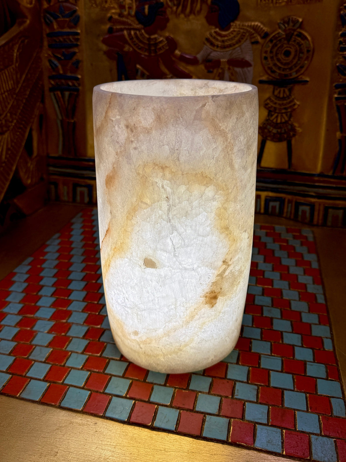 Slender cream alabaster cylinder vase with a rounded base and sweeping honey-coloured vein — full view.