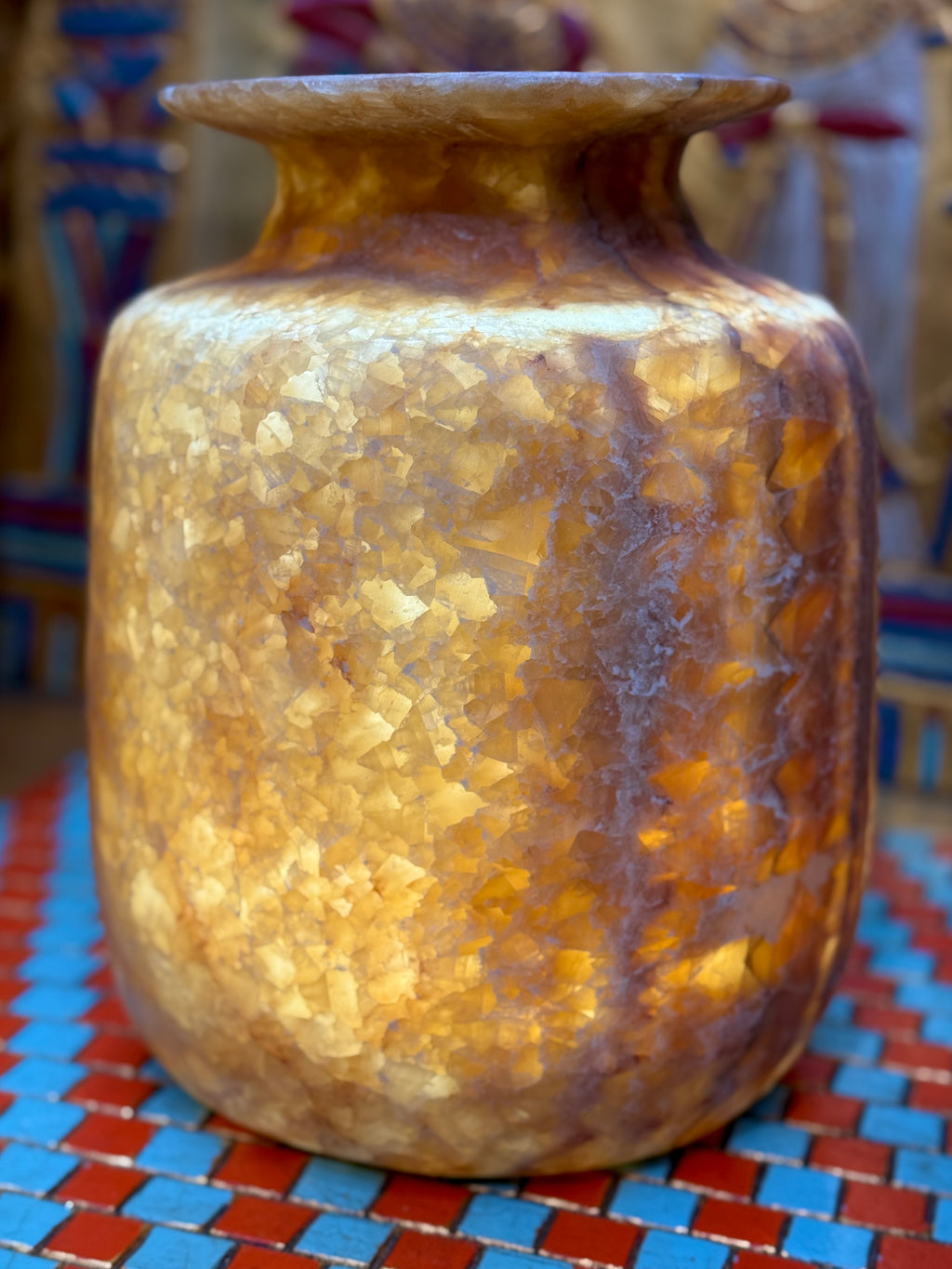 Squared alabaster vase with rounded corners, smoky brown stone, lighter vertical stripes and a flared rim — illuminated view showing amber-coloured stone.