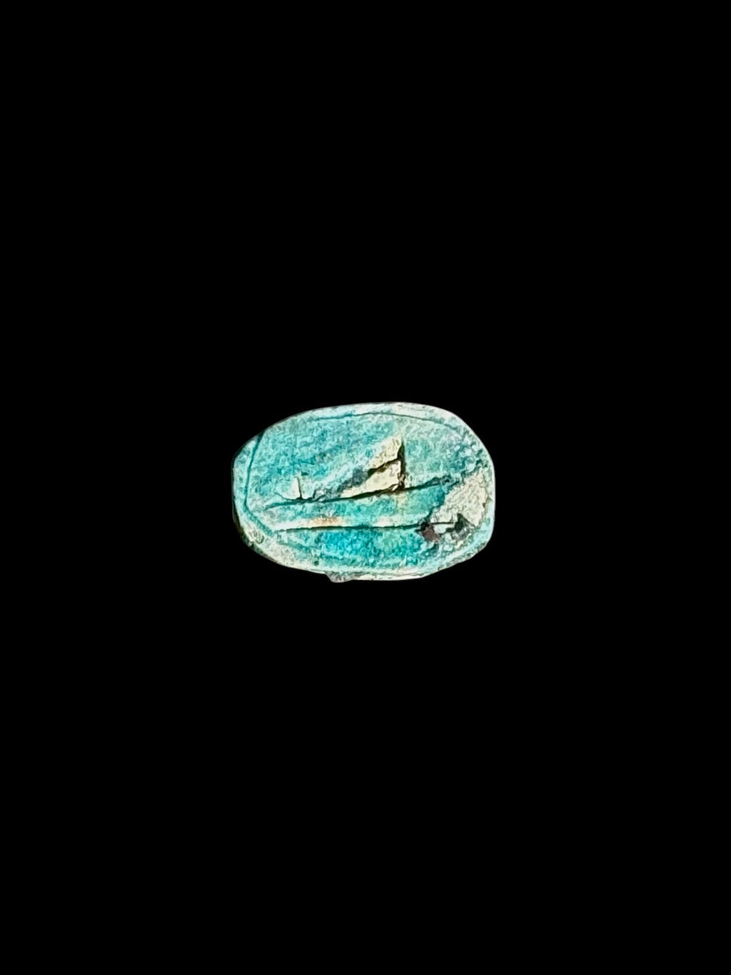 Underside of a turquoise-coloured stone scarab with incised markings, pale patches and an oval border against a black background.