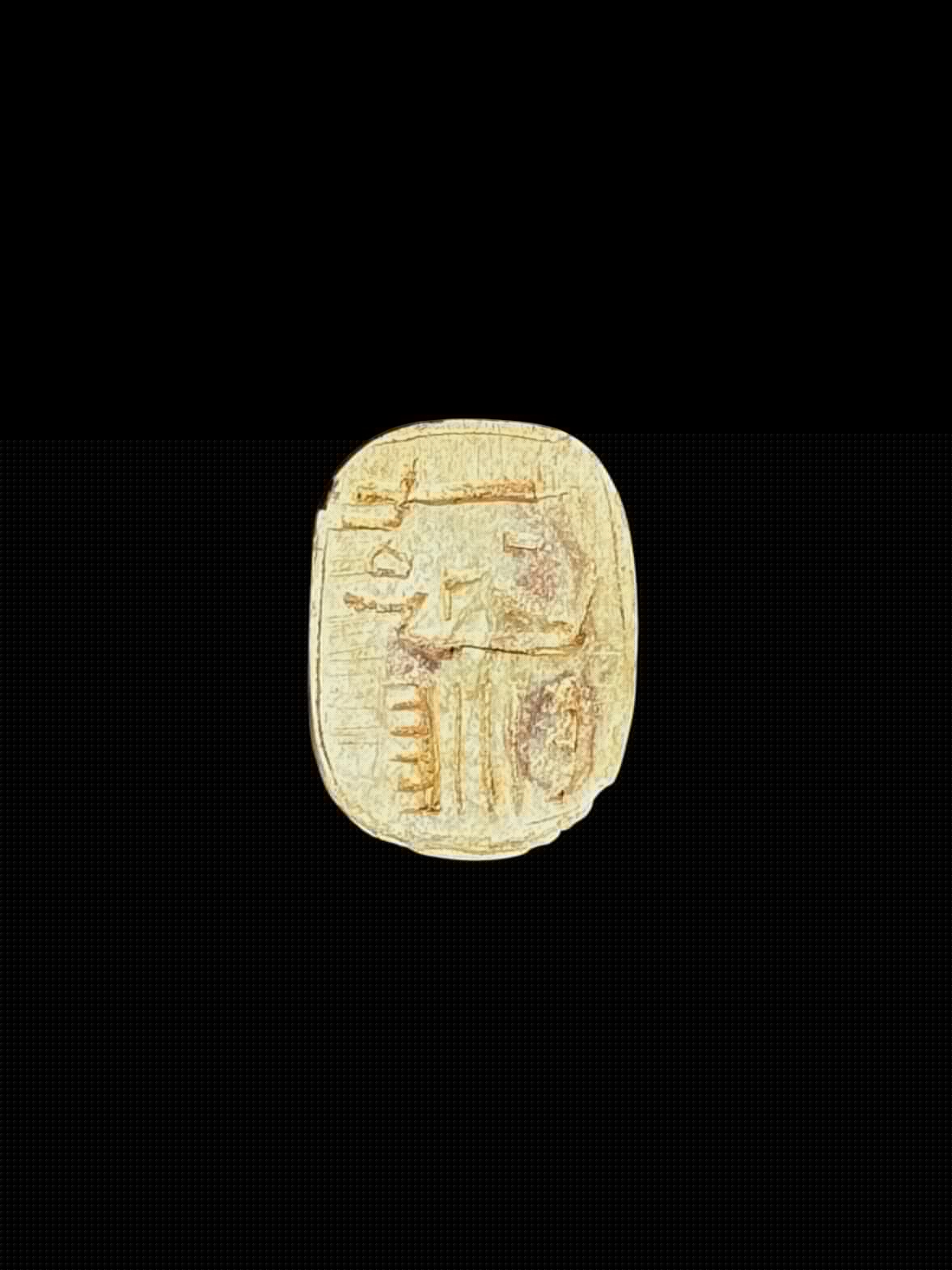 Underside of a pale cream and tan stone scarab showing incised markings within an oval border against a black background.