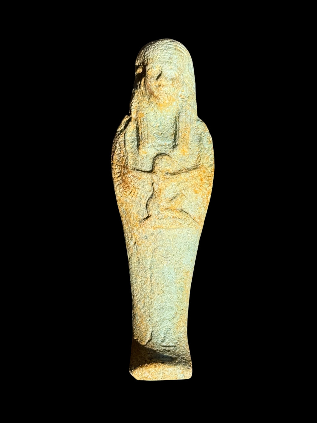 Front view of an Egyptian stone figurine with a winged Isis motif beneath a long headdress and textured blue-green and ochre colouring.