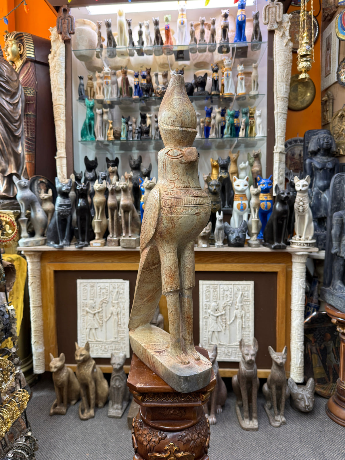 Full three-quarter view of the Horus falcon statue with tall crown, patterned chest, long legs and elongated base.