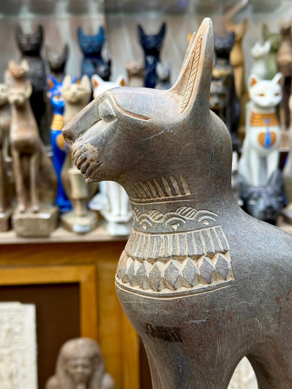 Side close-up of the Bastet statue's head and upper body, showing ear markings, outlined eye and patterned collar.