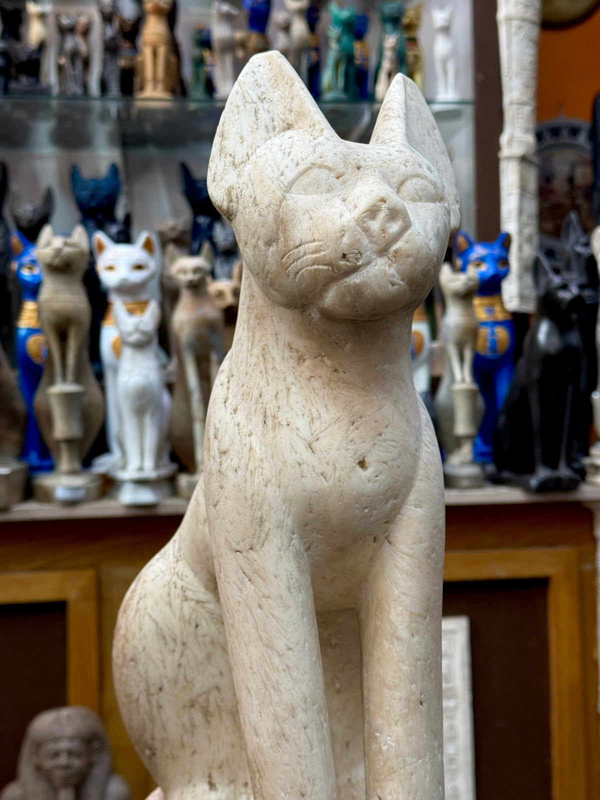Angled close-up of Bastet’s face and chest showing incised whiskers, beige and grey surface markings and small pits.