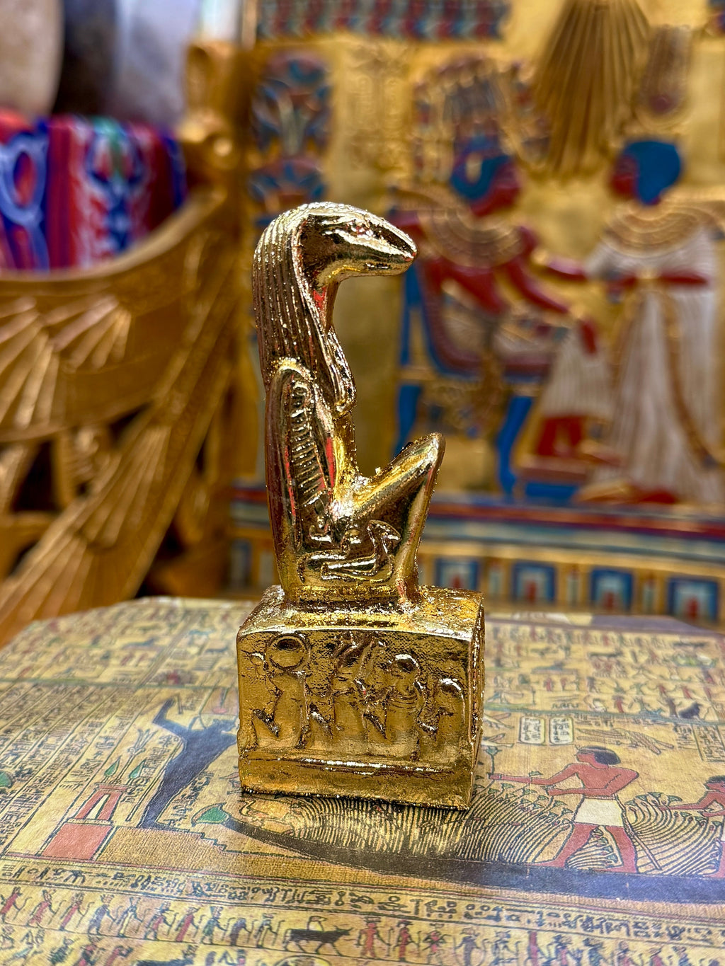 Side view of the gold finish Thoth kneeling statue with sculpted head, striped headdress and decorated square base.