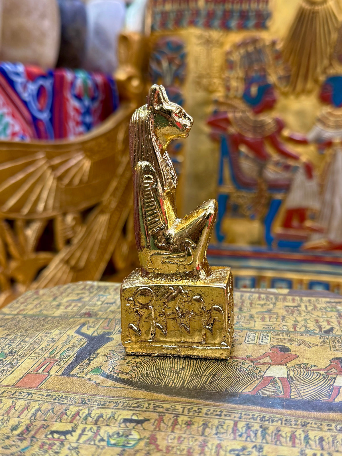Side view of the gold finish Bastet kneeling statue with cat head, pointed ears and decorated square base.