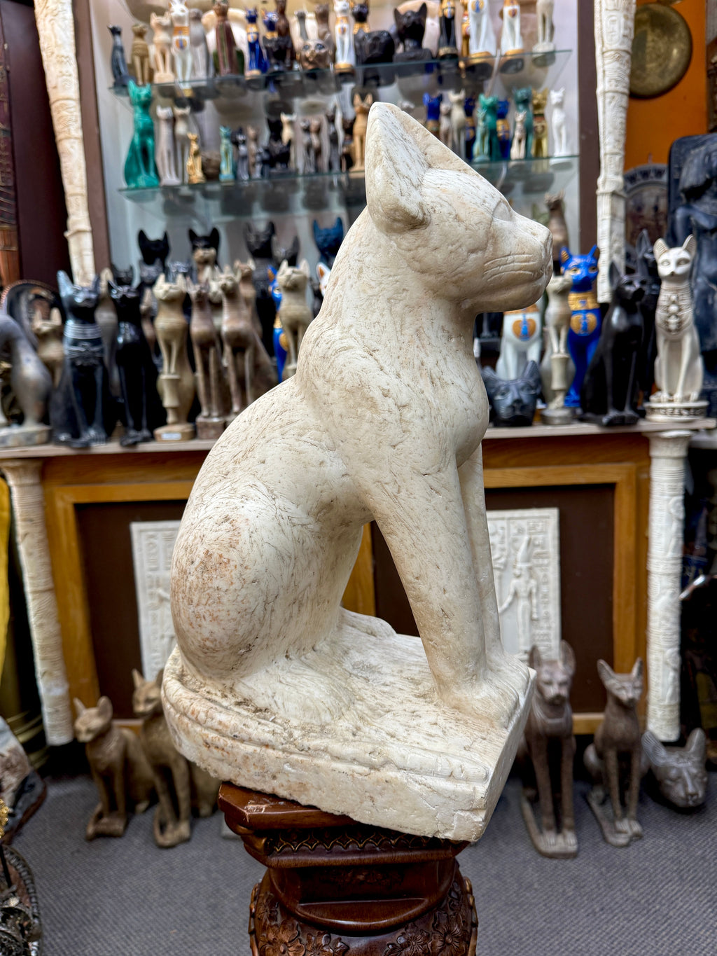 Side view of the seated Bastet statue facing right, showing rounded haunches and the tail curving along the base.