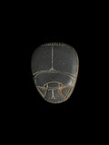 Dark grey stone scarab showing the beetle face, with pale incised wing and head outlines and brown-toned areas near the lower edges.