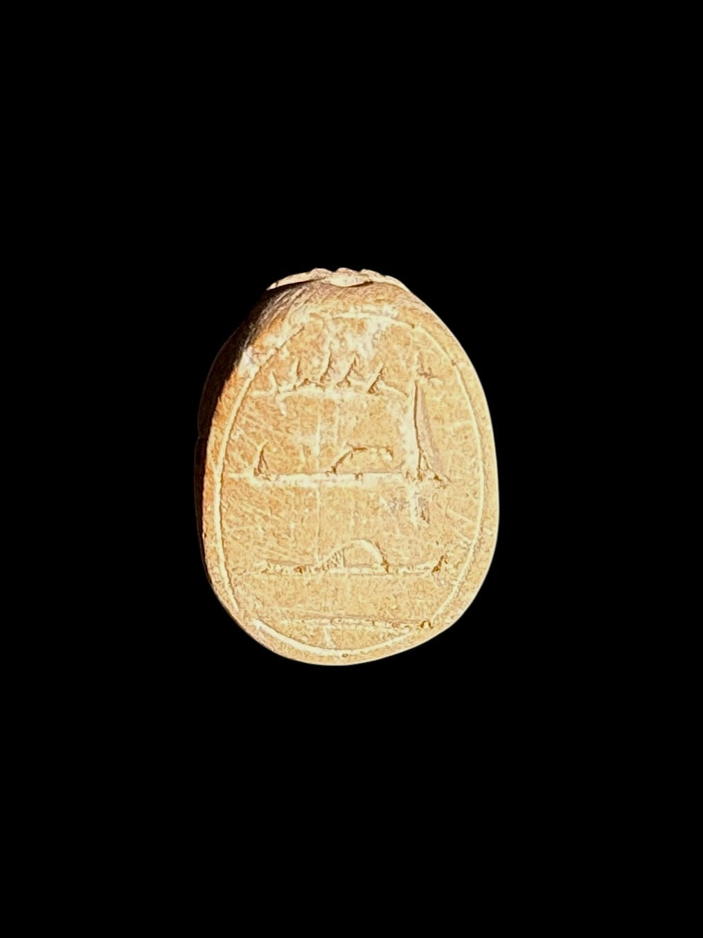 Underside of a cream and tan stone scarab showing shallow incised markings within an oval border against a black background.