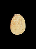 Underside of a cream and tan stone scarab showing shallow incised markings within an oval border against a black background.