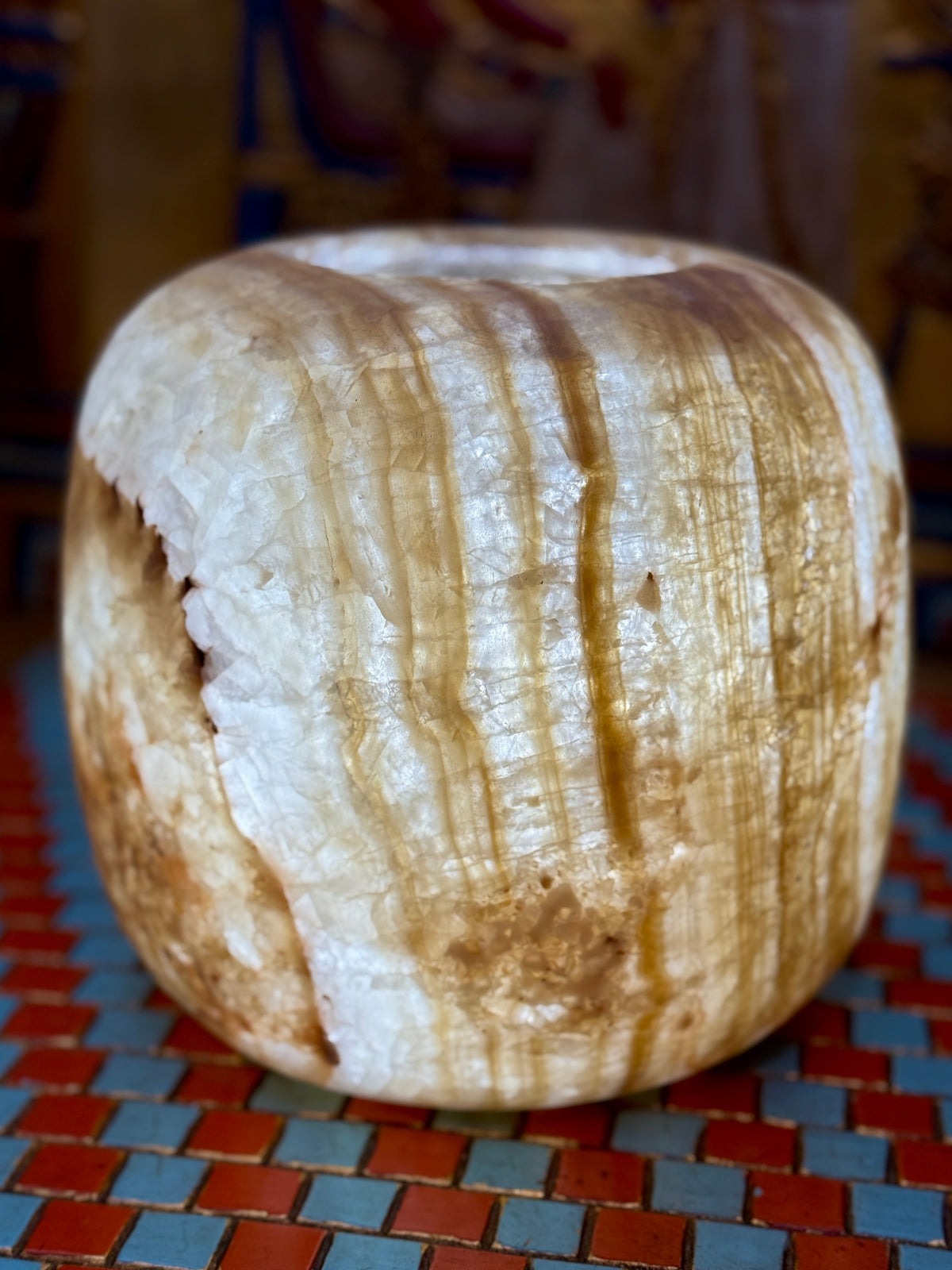 Broad cream alabaster vase with rounded shoulders, golden-brown vertical bands and a simple opening — illuminated view.