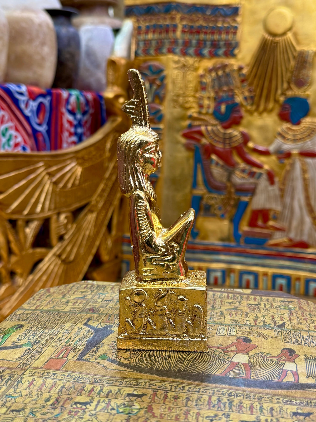 Side view of the gold finish Maat kneeling statue with tall feather headdress and decorated square base.
