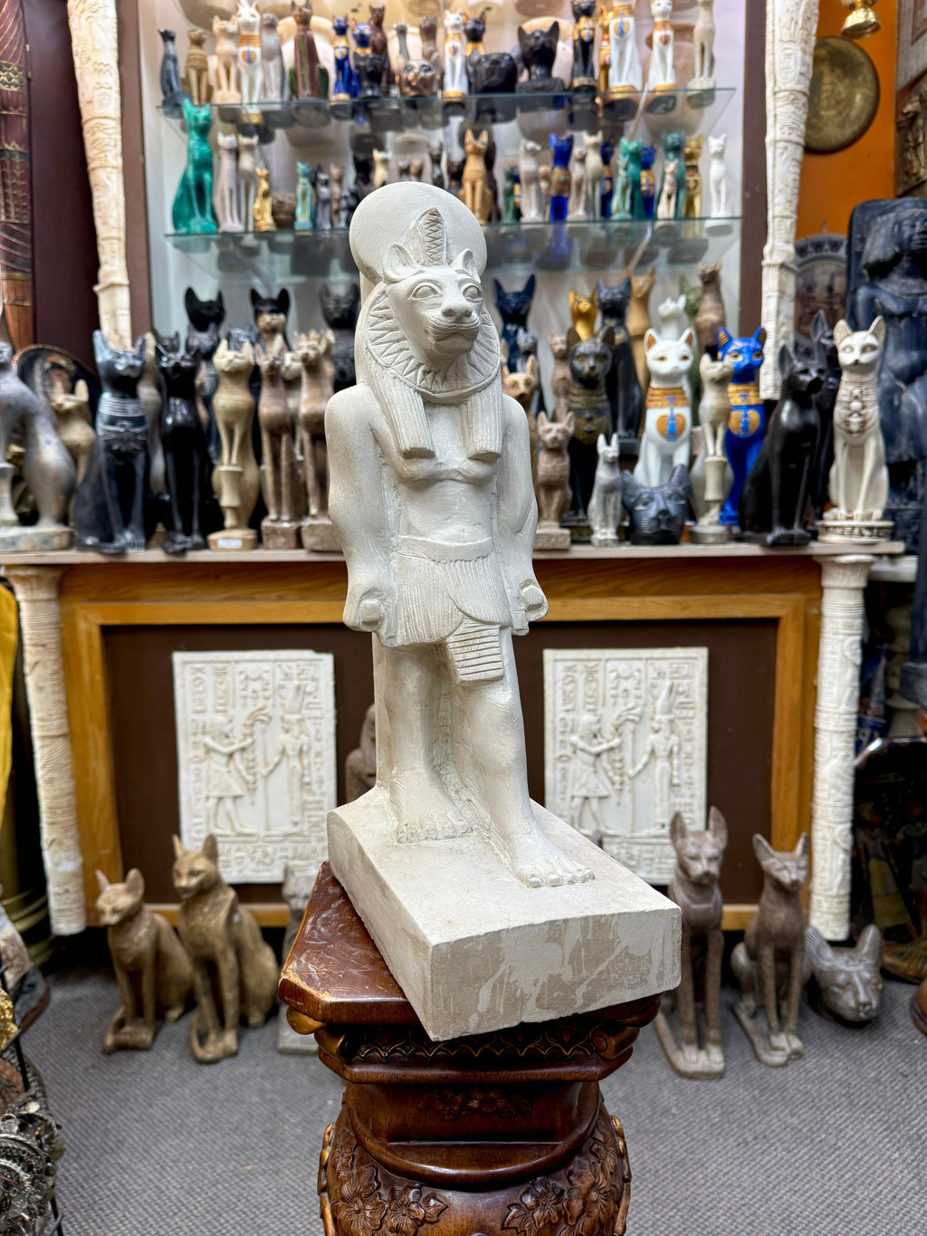 Full front view of pale cream Sekhmet statue with lioness head, sun disc and one foot forward on a rectangular base.