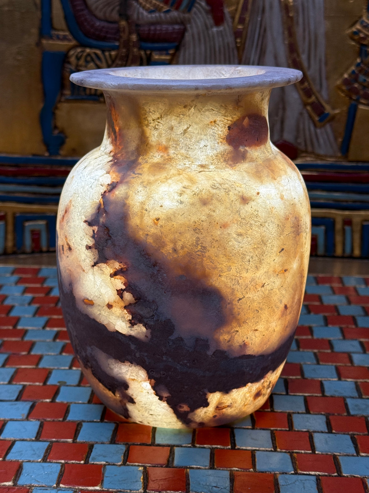 Rounded alabaster vase with a sweeping brown vein, narrow neck and flared rim — illuminated view.