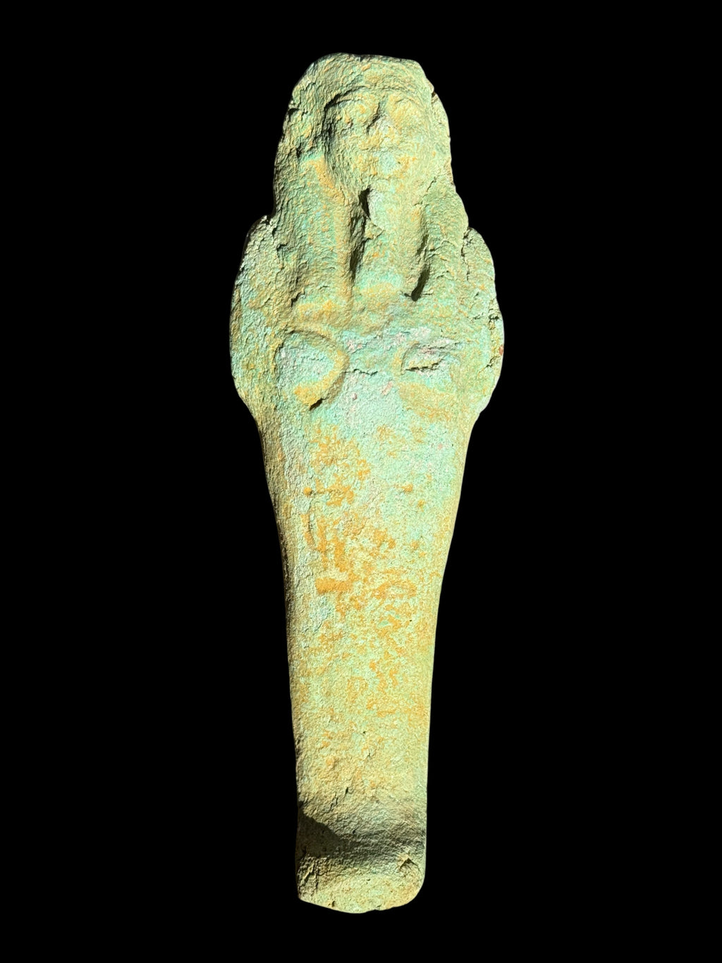 Front view of a shabti figurine with a pale green and ochre textured surface, headdress, long beard, crossed arms and tapering body.