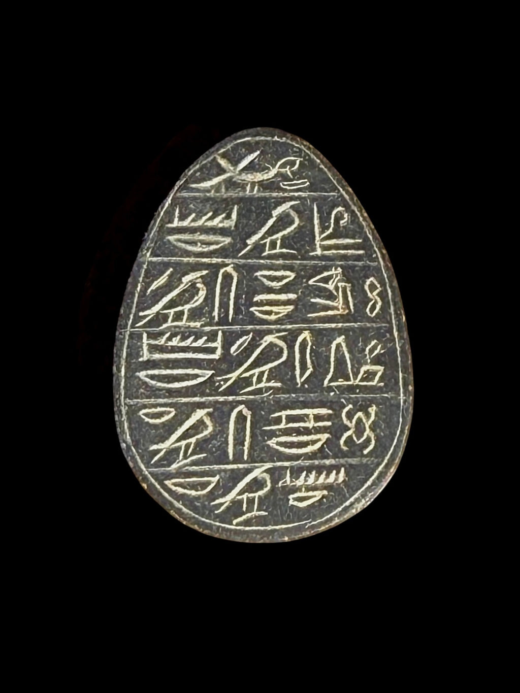 Reverse of the dark grey stone scarab, showing rows of pale hieroglyphic markings within an outlined border against a black background.