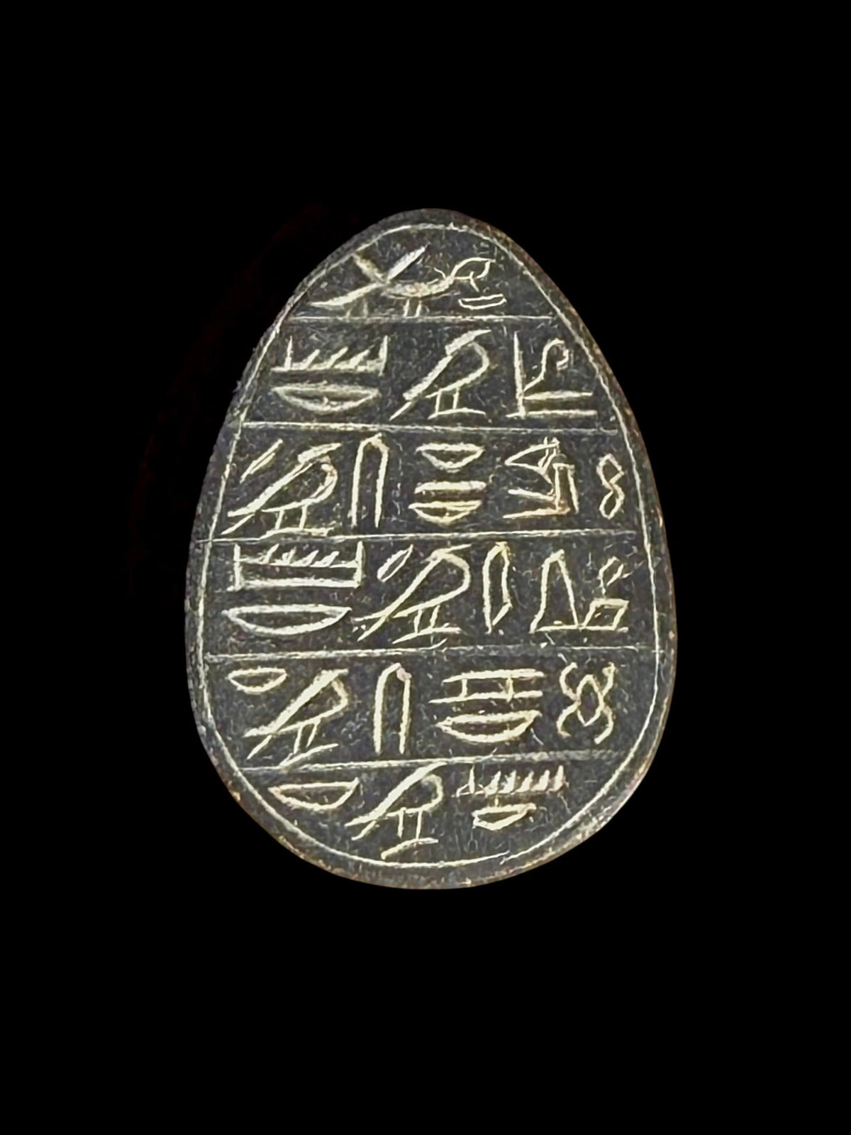 Reverse of the dark grey stone scarab, showing rows of pale hieroglyphic markings within an outlined border against a black background.