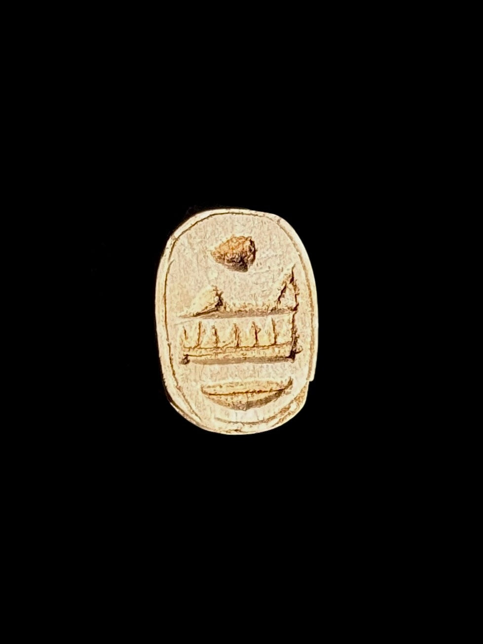 Cream and tan stone scarab underside with incised motifs inside an oval border, shown against black.