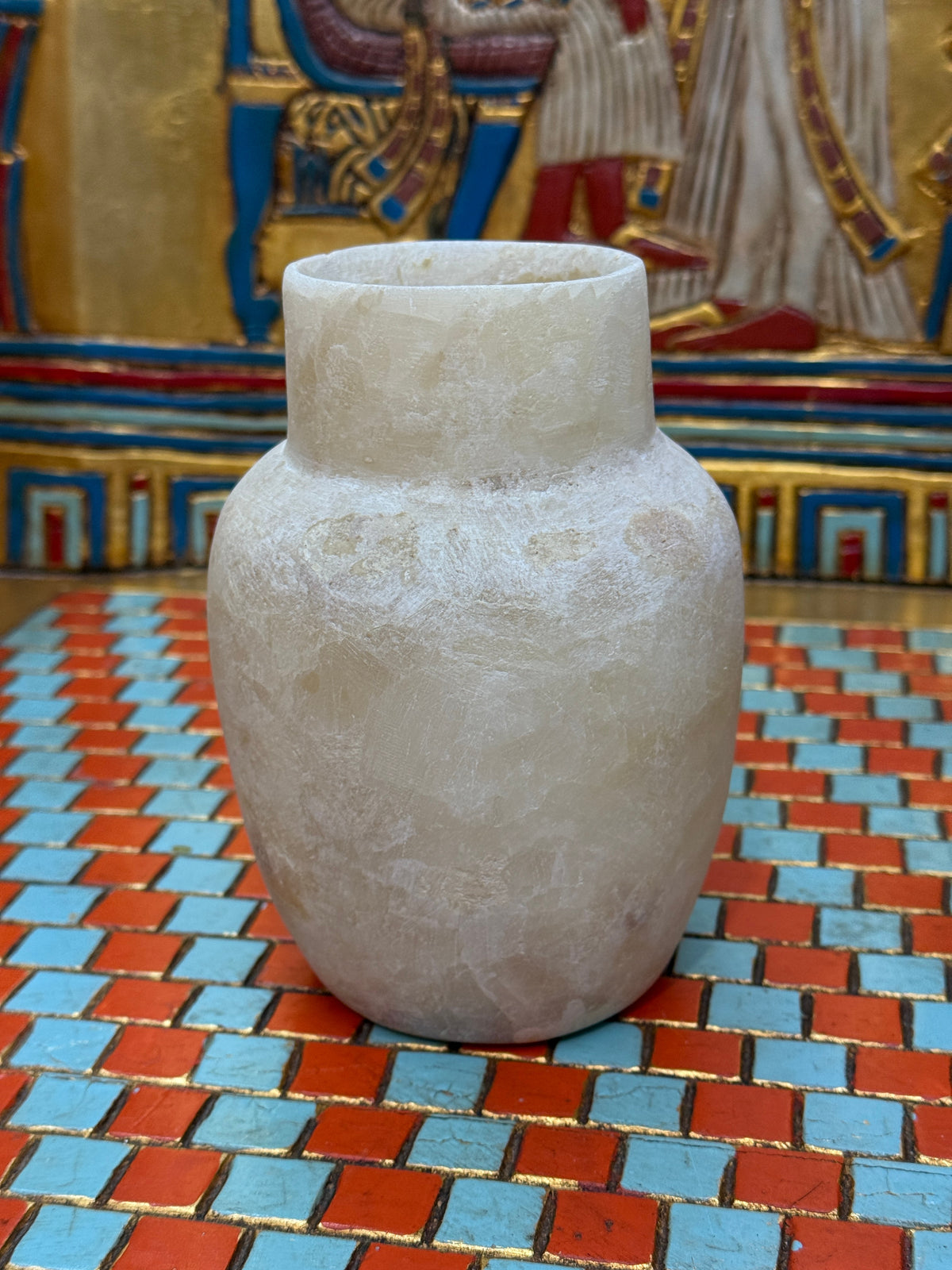 Small cream alabaster vase with a straight neck, rounded shoulders and a honey-coloured marking — unlit full view.