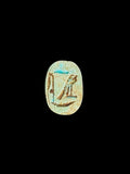 Pale cream-green oval underside of a stone scarab with incised markings, brown accents and turquoise patches against a black background.