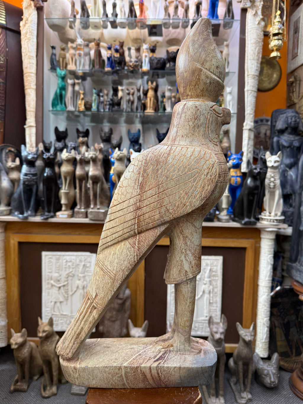 Side view of the crowned Horus falcon showing incised wing feathers, long tapered tail and elongated stone base.