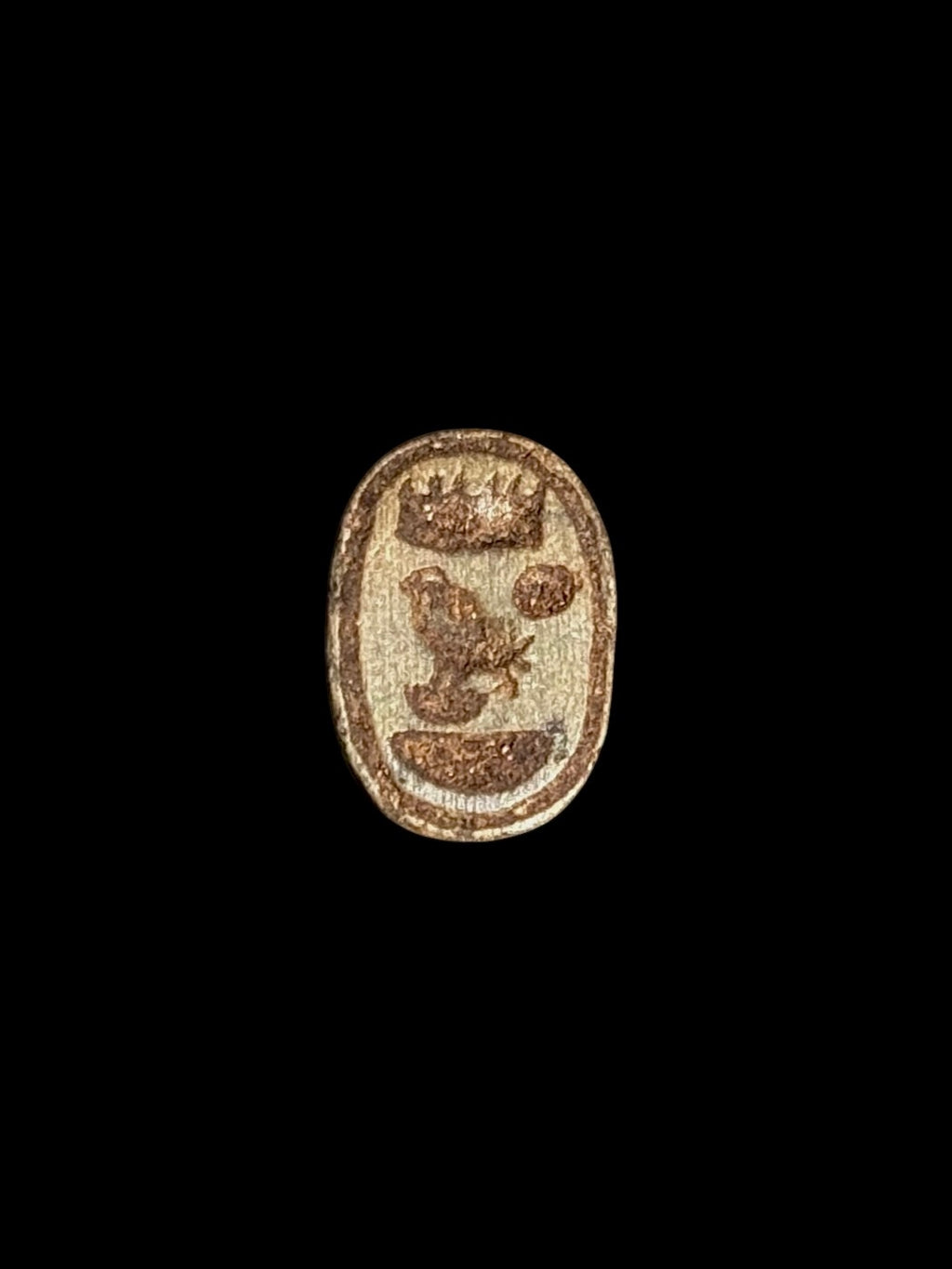 Oval underside of the stone scarab, showing brown markings including a bird-like figure and circular motif within a border.