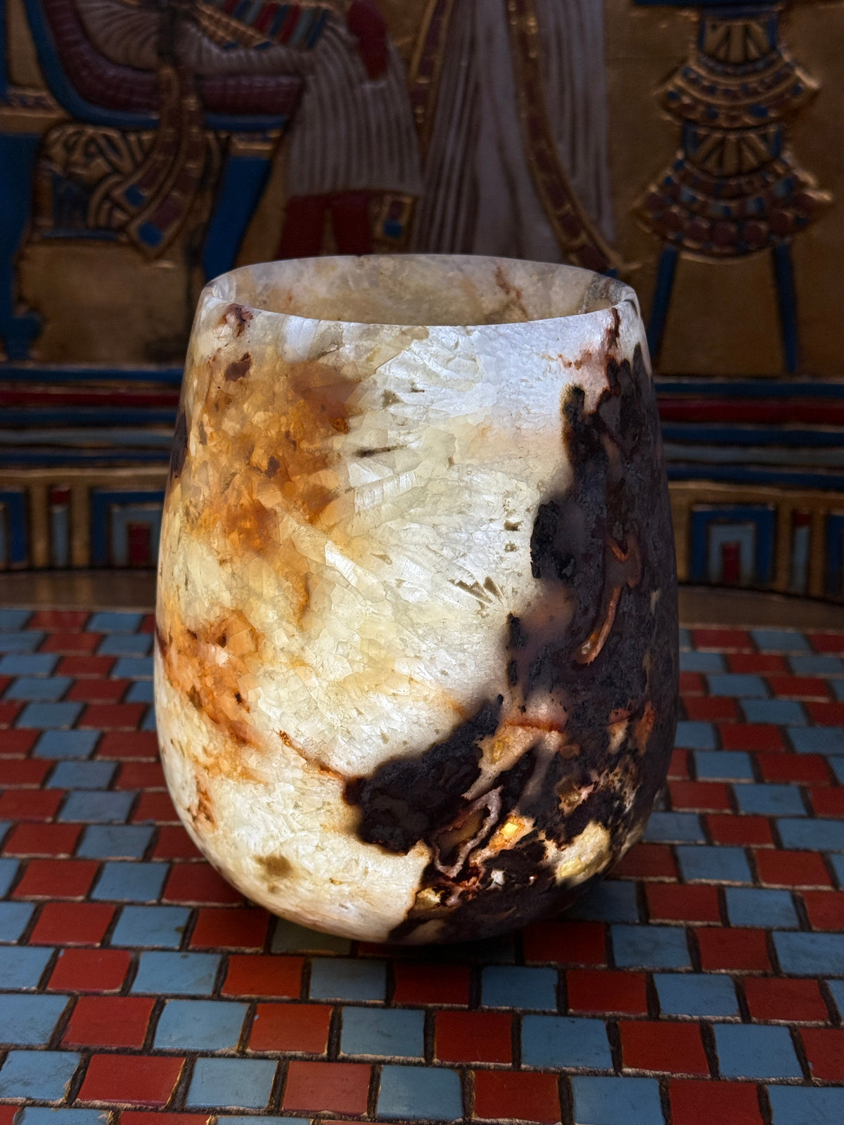 Compact curved alabaster vase with cream and taupe stone and contrasting brown markings — illuminated view.