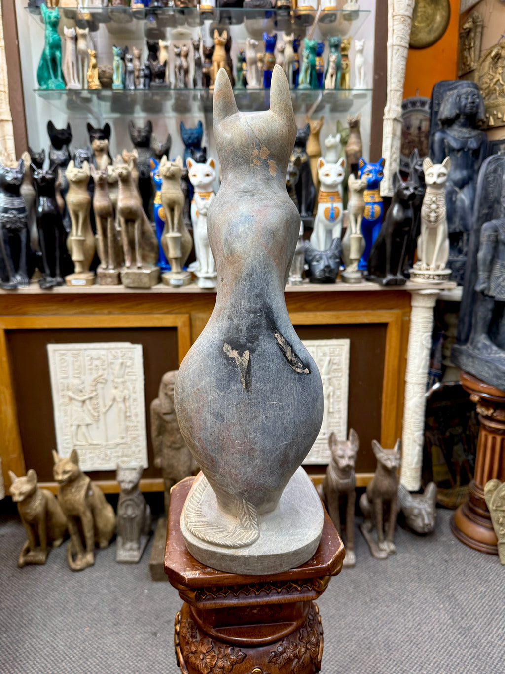Rear view of the Bastet statue showing upright ears, a narrow back, rounded haunches, dark and pale surface patches, and curved tail.