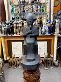 Front view of a dark seated Osiris statue with feathered crown, crossed arms, inscribed throne and extended base.