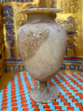 Cream alabaster pedestal vase with an oval body, slender stem, round foot and flared rim — unlit full view.