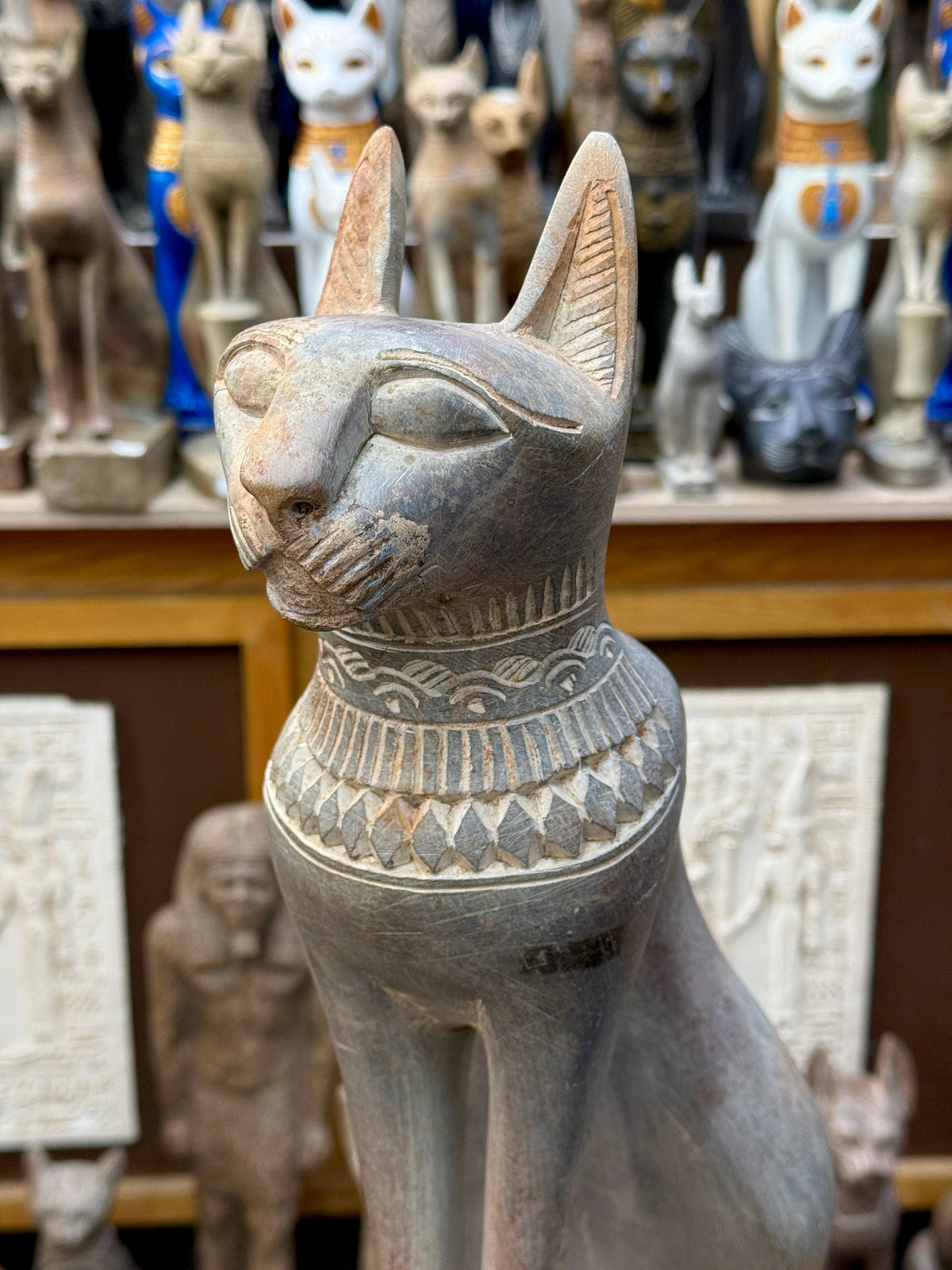 Close front view of the Bastet statue's outlined eyes, incised whiskers, tall ears and layered geometric collar.