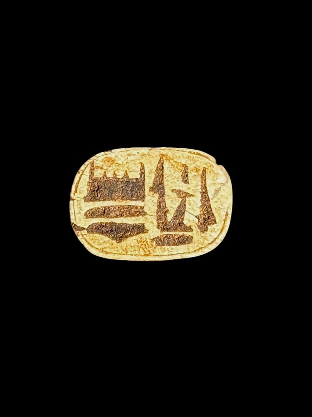 Underside of the stone scarab showing brown recessed markings within an oval border on a cream-coloured surface.