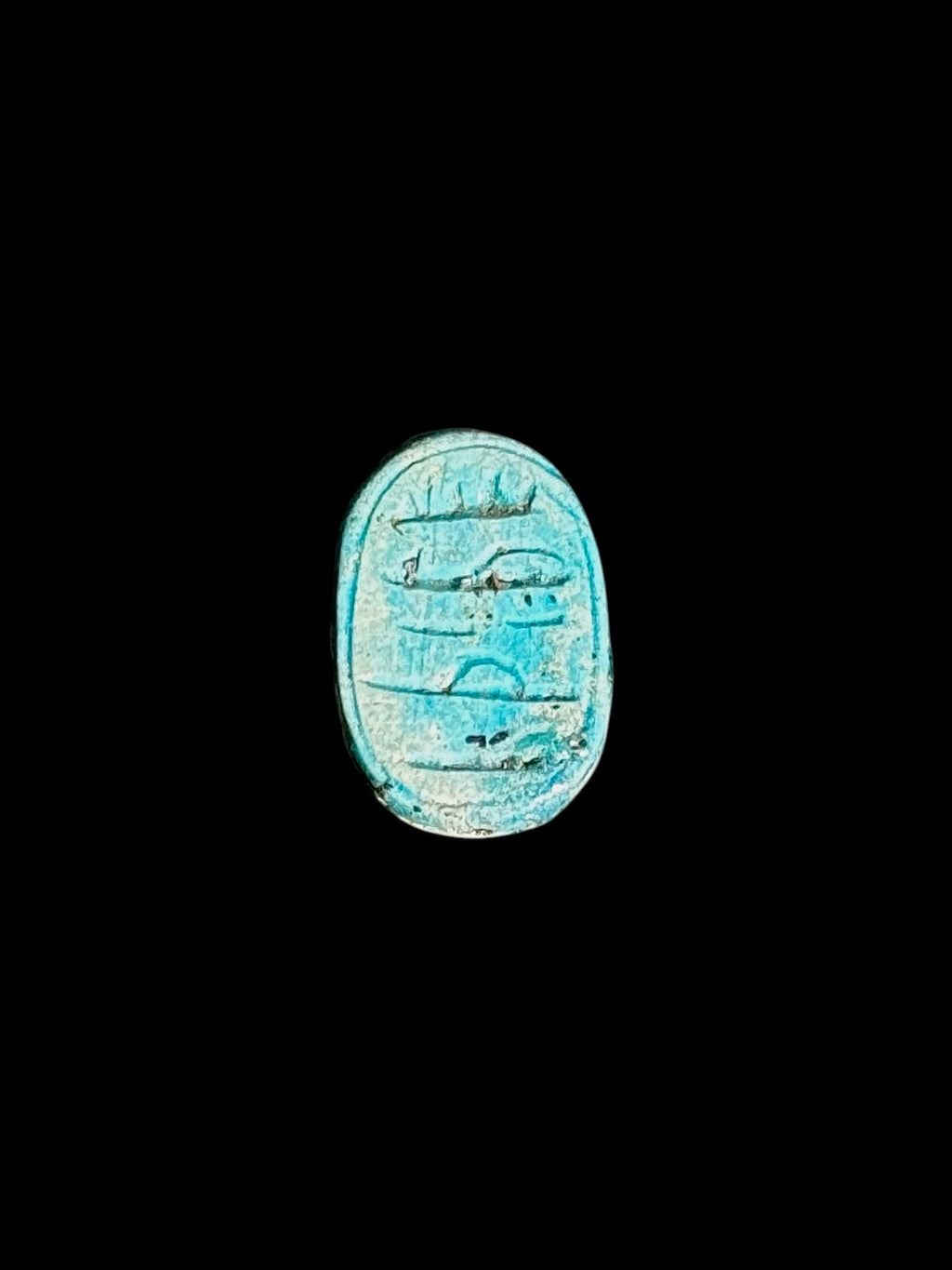Oval underside of a turquoise-coloured stone scarab with incised markings, a recessed border and pale surface mottling.