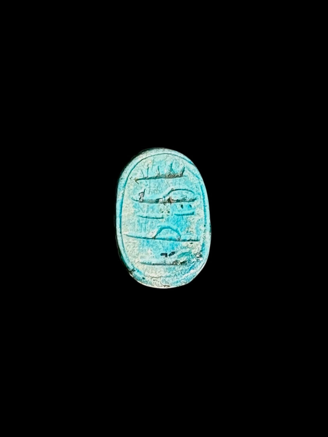 Oval underside of a turquoise-coloured stone scarab with incised markings, a recessed border and pale surface mottling.
