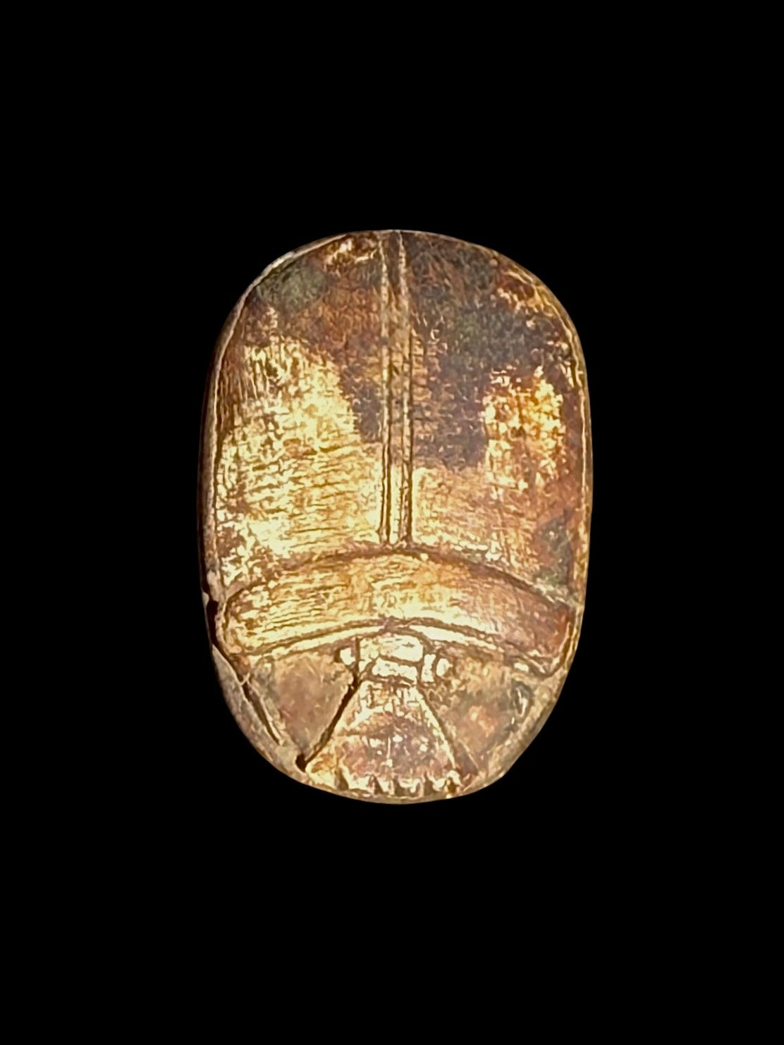 Top view of a gold-coloured stone scarab with a central wing division, curved head details and darker surface recesses.