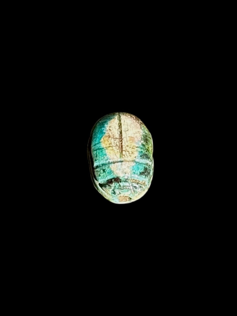 Upper view of an oval stone scarab with incised beetle details and mottled turquoise, cream and brown colouring on a black background.