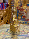 Front angled view of the gold finish Anubis kneeling statue with jackal head, upright ears and decorated square base.