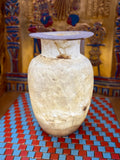 Tall pale alabaster vase with branching brown veins, an upright neck and flared rim — full view.