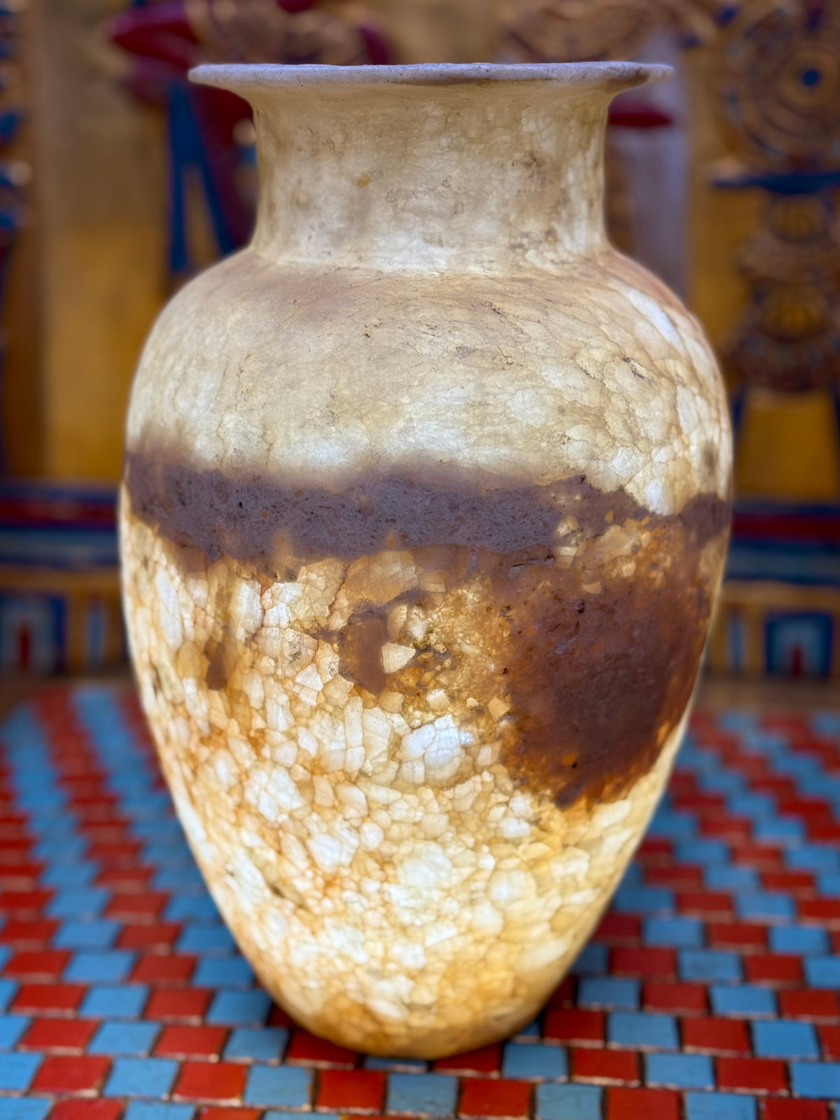 Alabaster vase with a pale upper body, broad earthy band, rounded shoulders and flared neck — illuminated view.